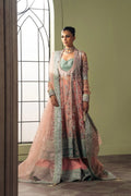 A woman models a traditional Indian ethnic wear set consisting of a pink and mint green embroidered kurta, matching dupatta, and a light green embroidered jacket. She is standing in a room with a large arched window on the left and a sage green wall behind her.