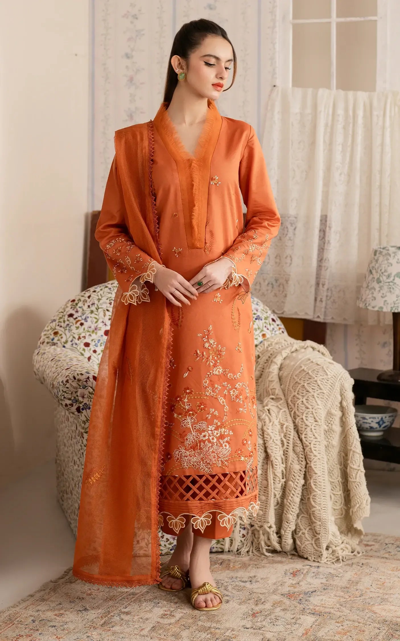 Woman in an orange traditional outfit sitting on a decorative chair.