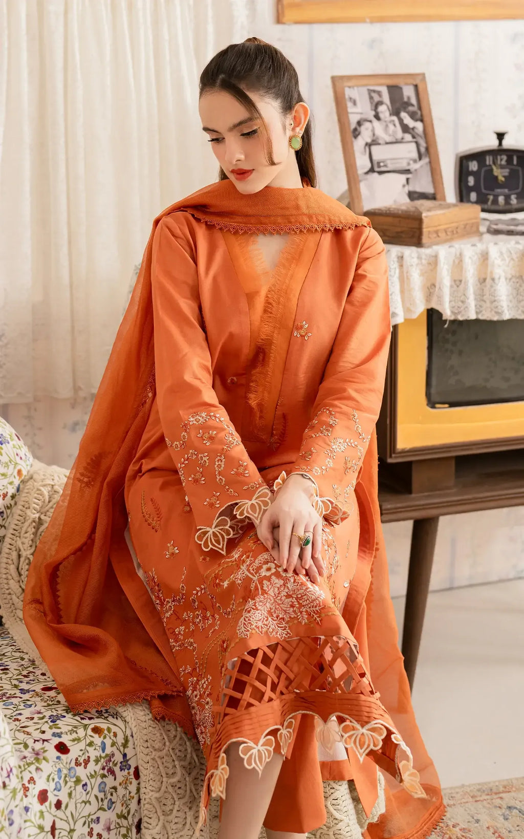 Woman in an orange traditional outfit sitting on a couch in a living room.