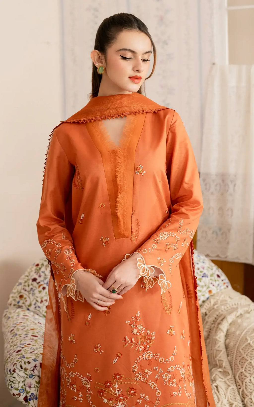 Woman wearing an orange embroidered traditional outfit with a neutral background