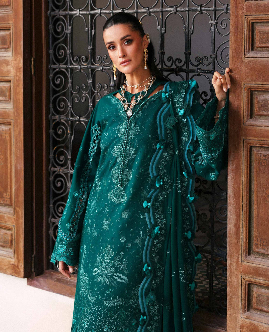 Woman in a teal embroidered dress standing in a doorway.