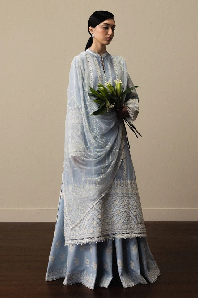 Woman wearing a light blue embroidered traditional outfit holding flowers against a plain background