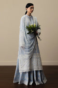 Woman wearing a light blue embroidered traditional outfit holding flowers against a plain background