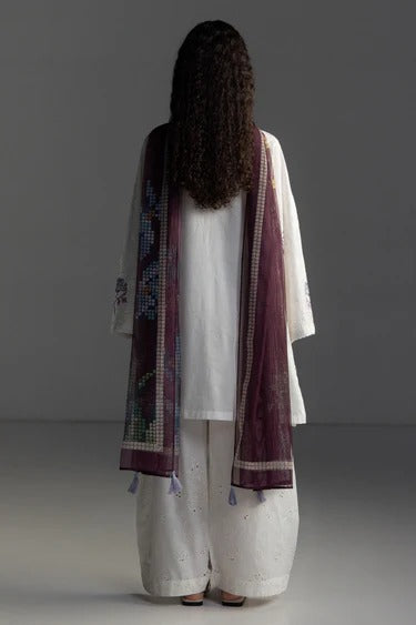 Person wearing a white outfit with a purple embroidered shawl on a gray background