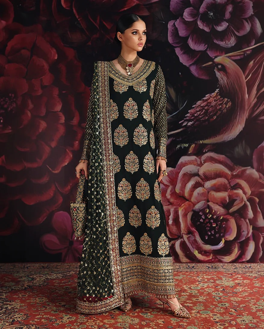 A woman models a traditional black embroidered kurta set with intricate gold and silver mirror-work patterns, set against a dark floral backdrop and a red patterned rug.