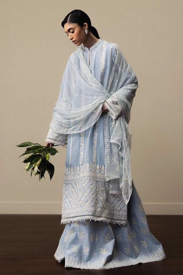 Woman wearing a light blue embroidered traditional outfit against a beige background