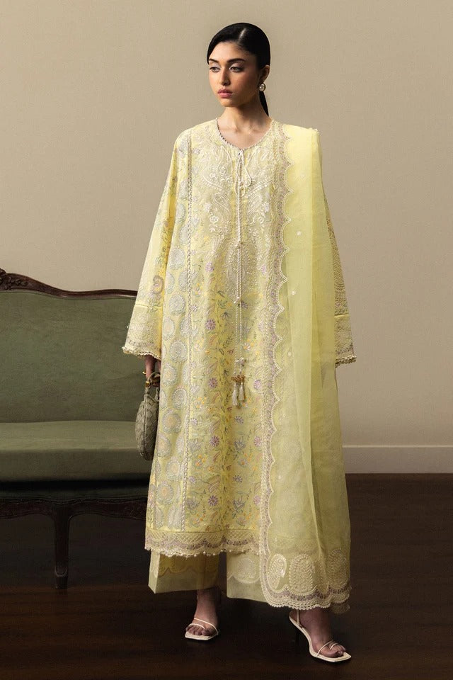 Woman wearing a light yellow embroidered traditional outfit in a room with a green sofa.