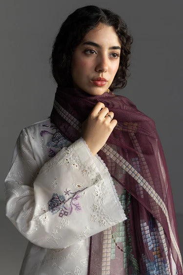 Woman wearing a white embroidered garment and a patterned scarf against a gray background