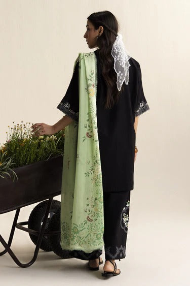 Woman holding a wheelbarrow with plants, wearing a black outfit and green floral scarf.