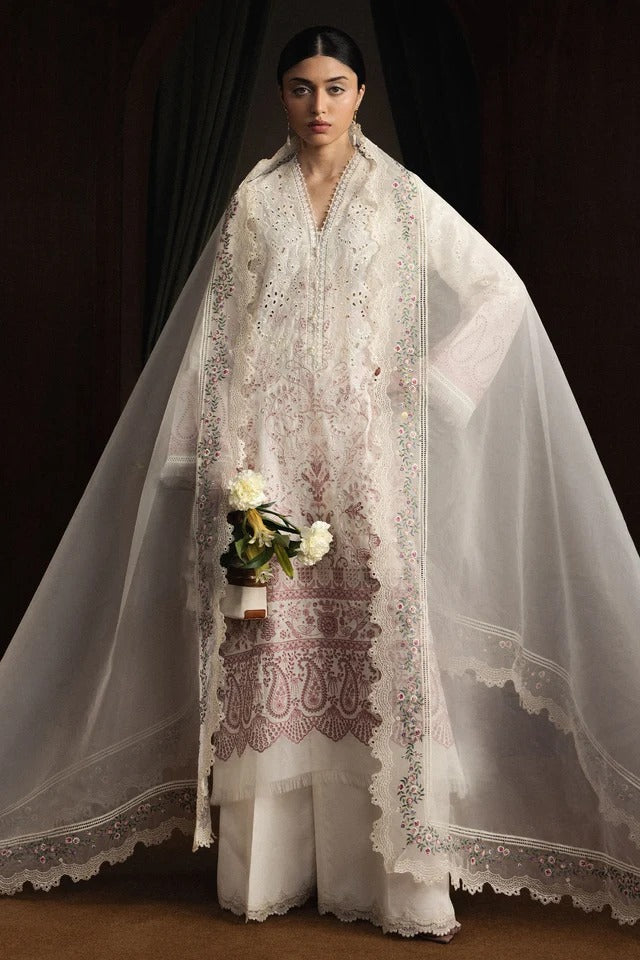 Woman wearing a white embroidered outfit with a sheer dupatta against a dark background