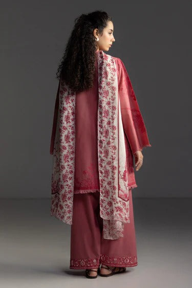 A woman modeling a traditional three-piece salwar kameez suit in dusty rose pink, featuring a matching printed dupatta and wide-leg trousers, photographed against a dark gray studio background.