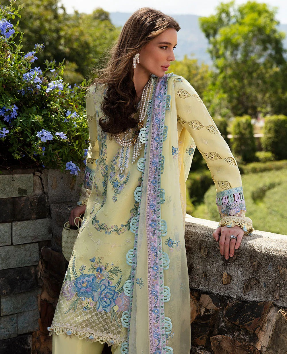 Woman in a light yellow embroidered outfit with floral patterns, standing outdoors with greenery in the background.