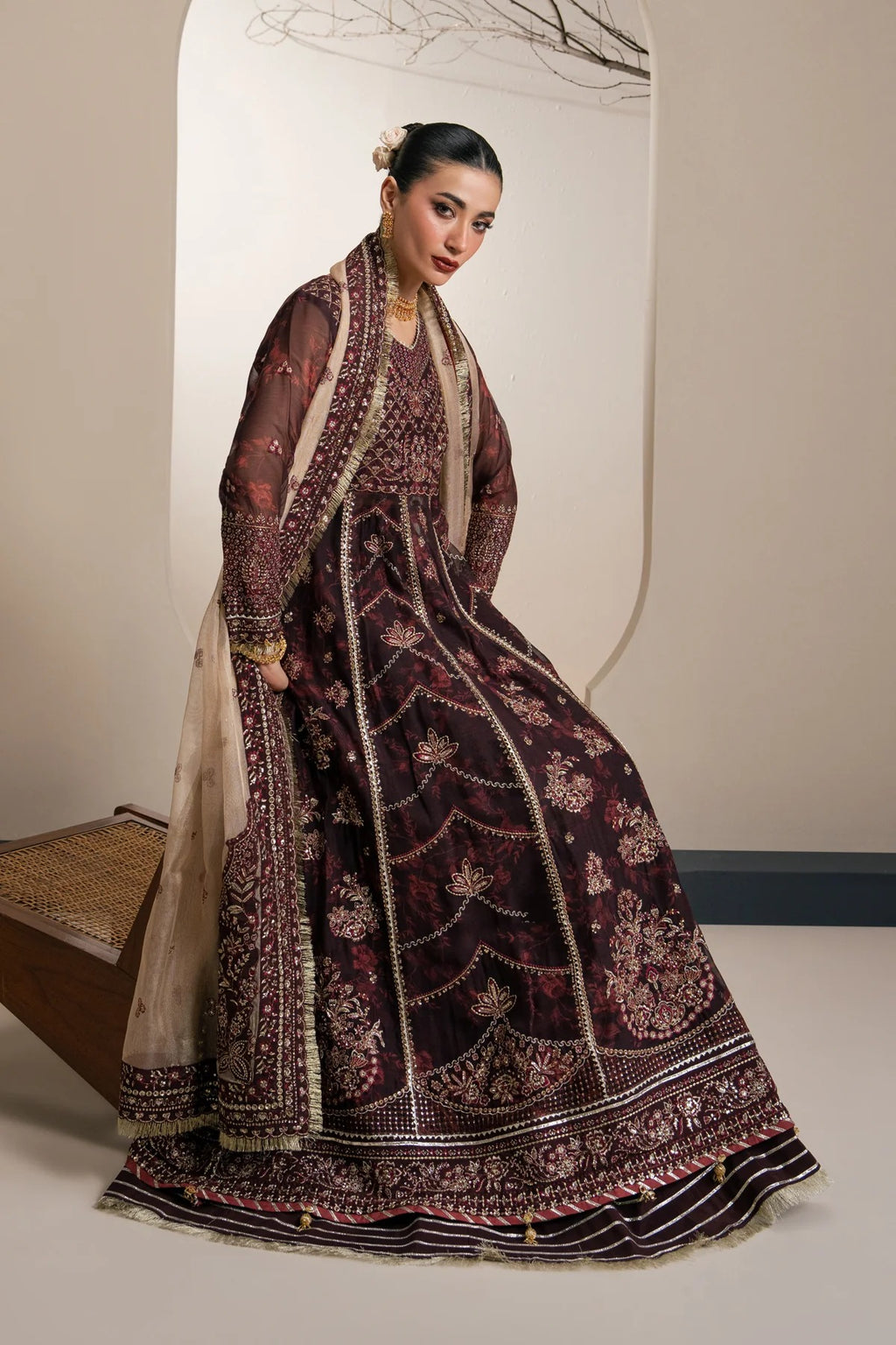 A woman models a traditional dark plum embroidered Anarkali gown with a beige dupatta in a studio setting.
