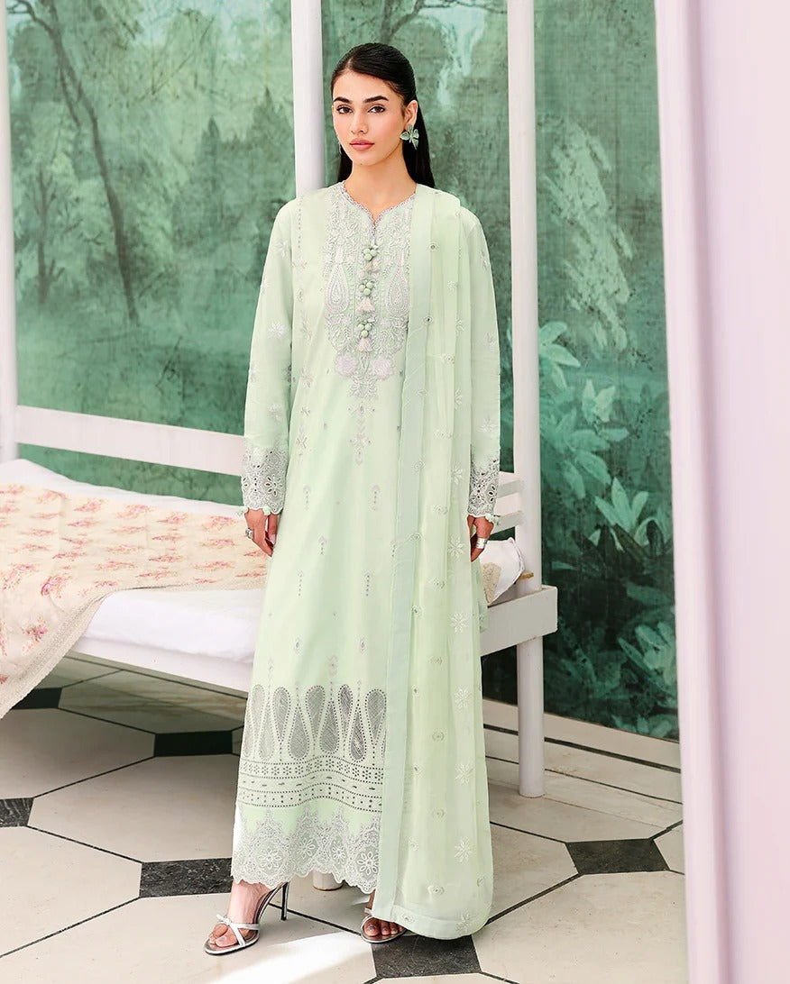Woman in a light green dress with white embroidery standing in a room with green walls and a bench.
