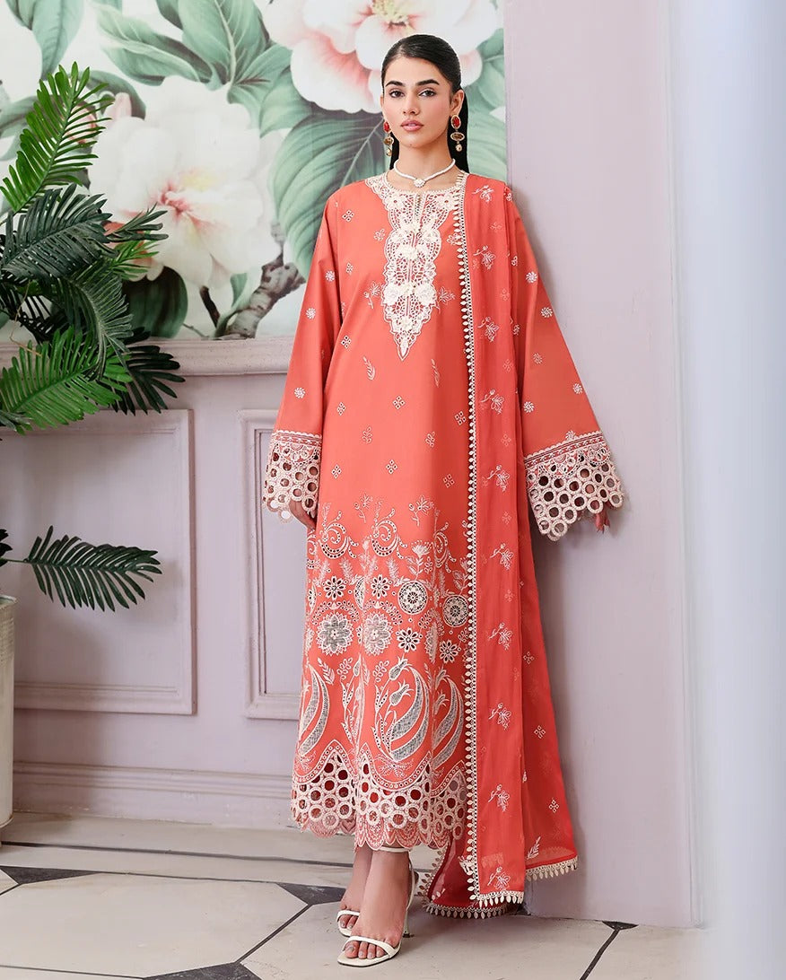 A woman models a peach-colored traditional kurta set with intricate white and silver embroidery, featuring a matching dupatta, set against a light pink wall with a floral print and potted plants.