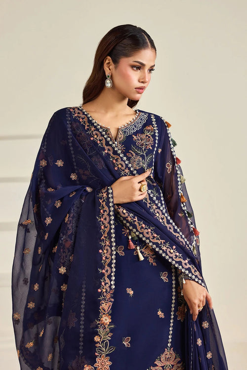A woman modeling a navy blue traditional outfit with intricate gold and peach floral embroidery, paired with a matching sheer dupatta, against a light beige background.