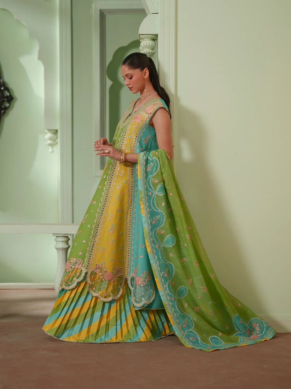Woman wearing a colorful traditional outfit with a green and yellow dress in a room.
