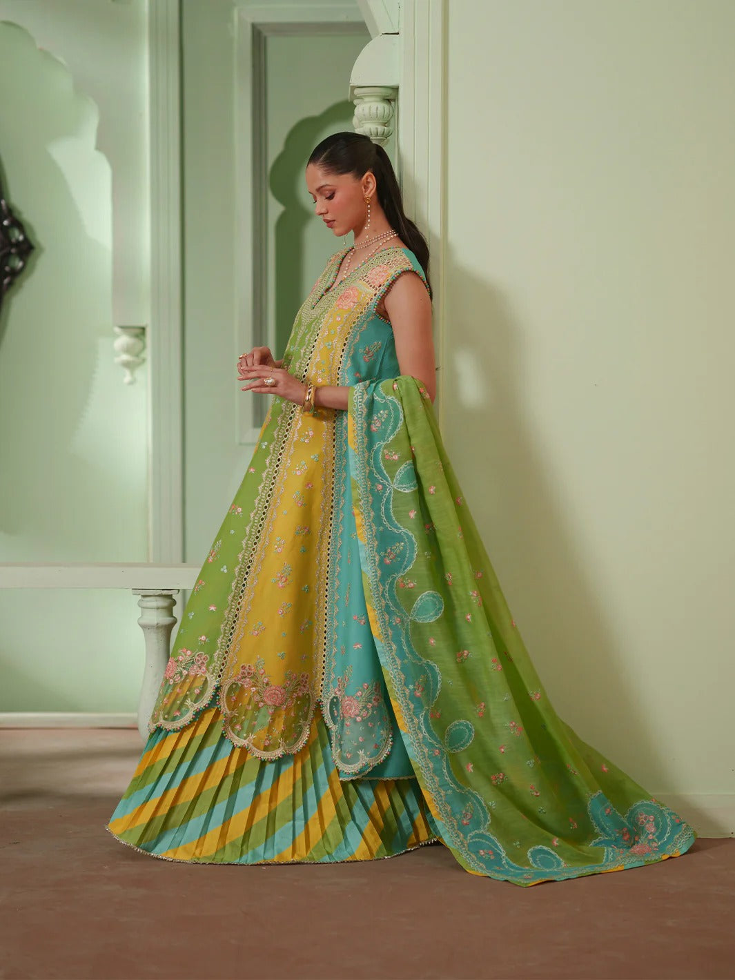Woman wearing a colorful traditional outfit with a green and yellow dress in a room.