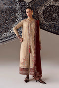 A woman models a traditional beige embroidered kurta set with a deep maroon dupatta, standing against a backdrop of patterned rugs.