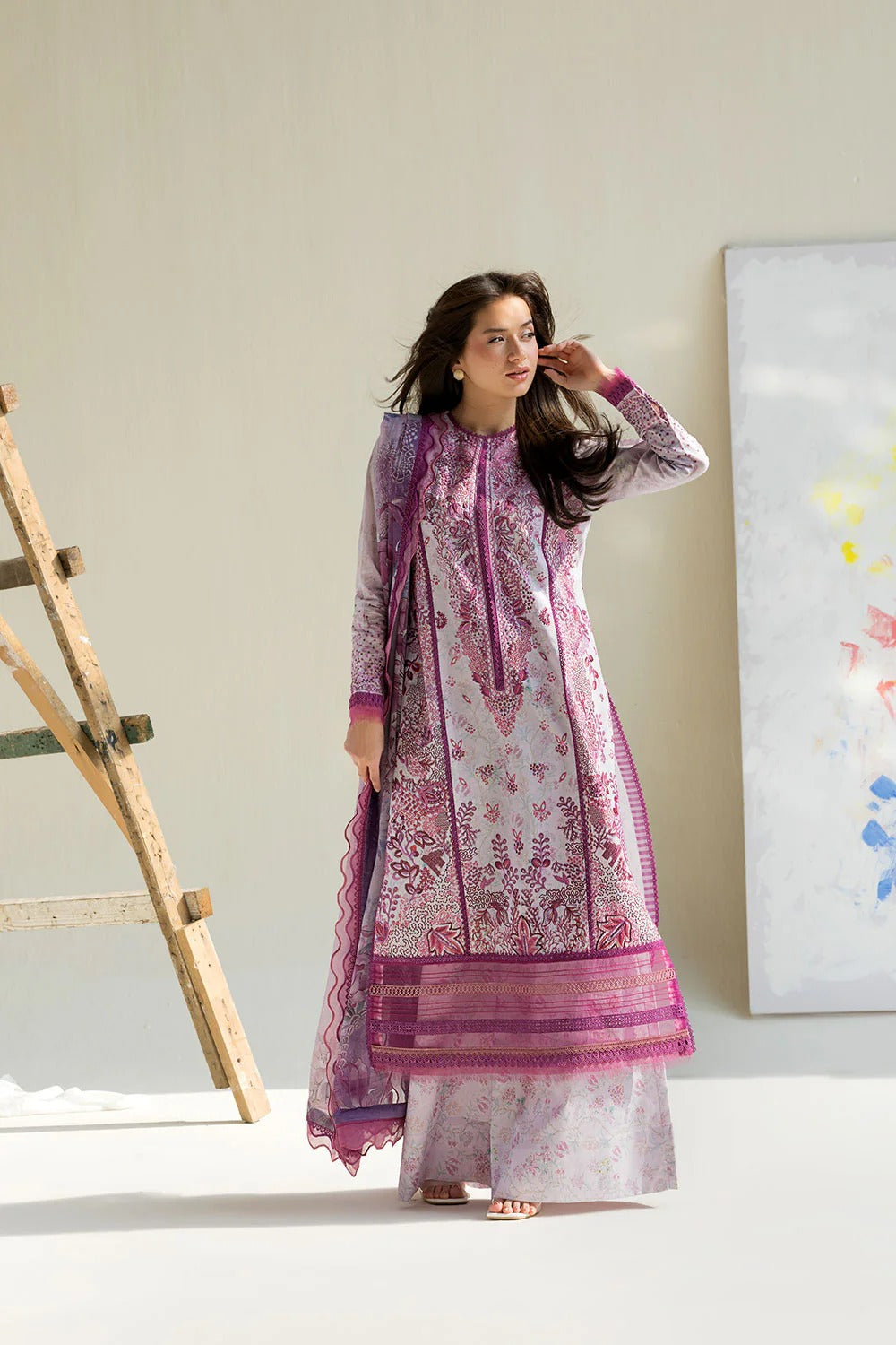 Woman wearing a traditional outfit with pink and white patterns in a minimalistic setting.