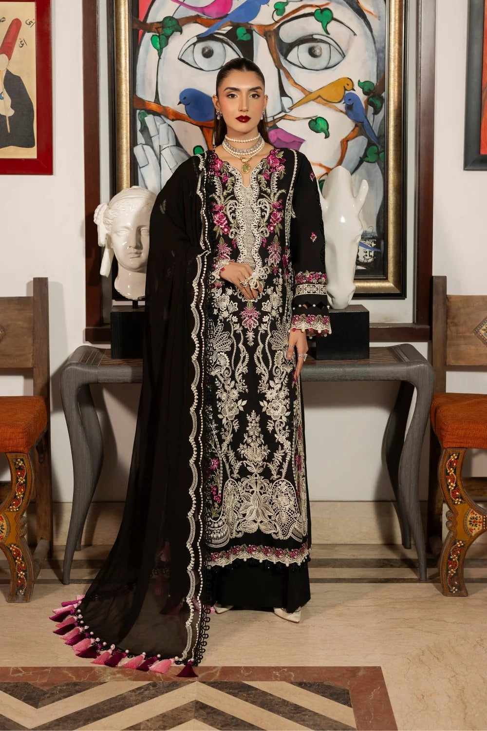 Woman in traditional black and white embroidered outfit standing in a room with artistic decor.