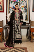 Woman in traditional black and white embroidered outfit standing in a room with artistic decor.