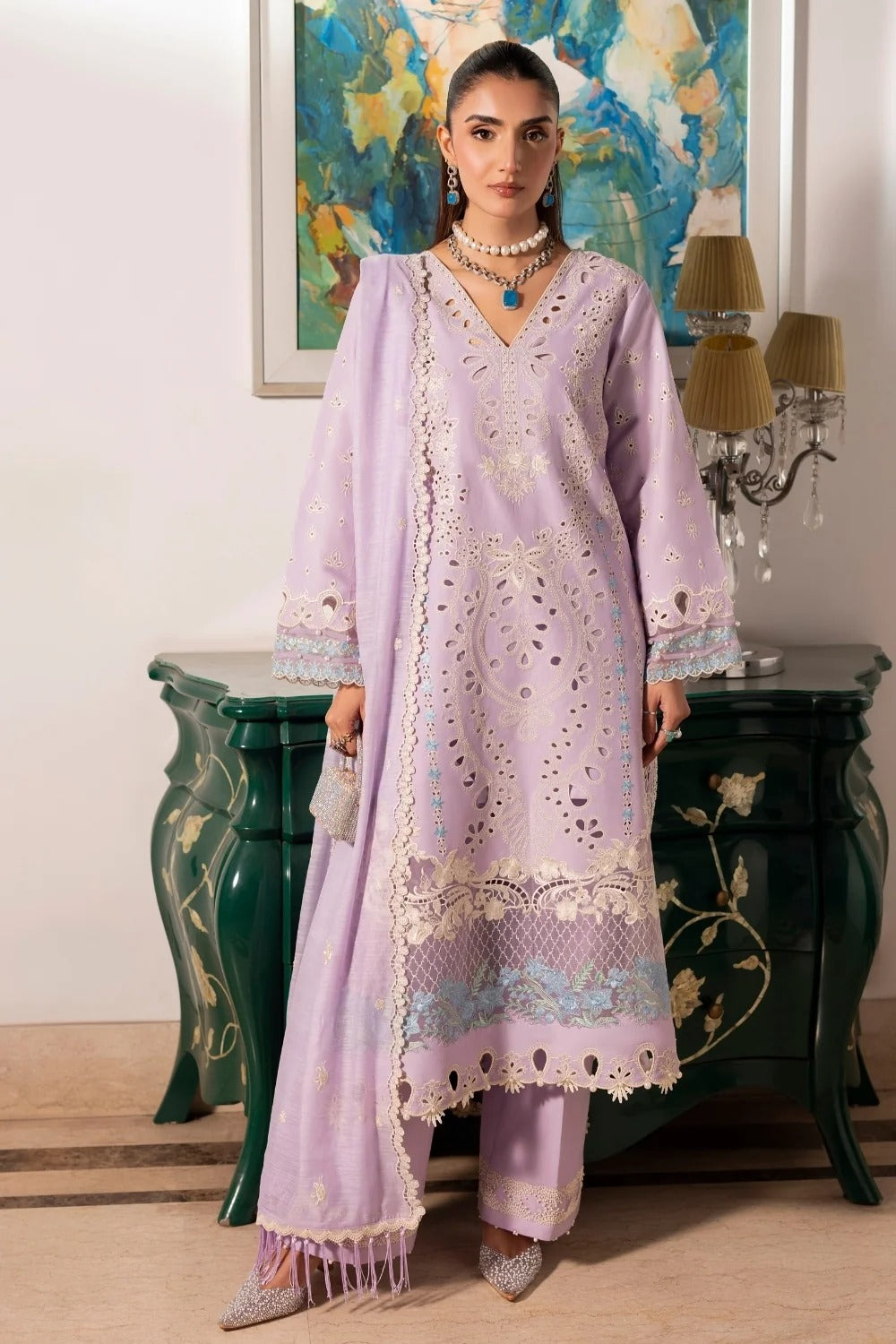Woman in a light purple embroidered outfit standing in a room with decorative elements.
