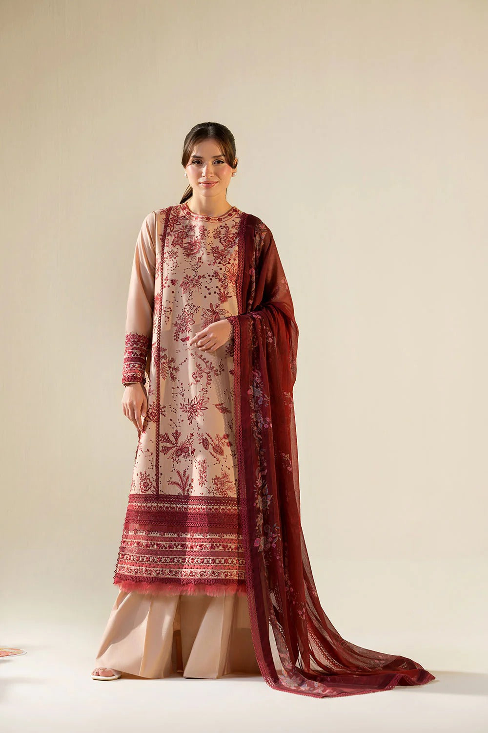 Woman wearing a traditional outfit with a maroon dupatta on a beige background