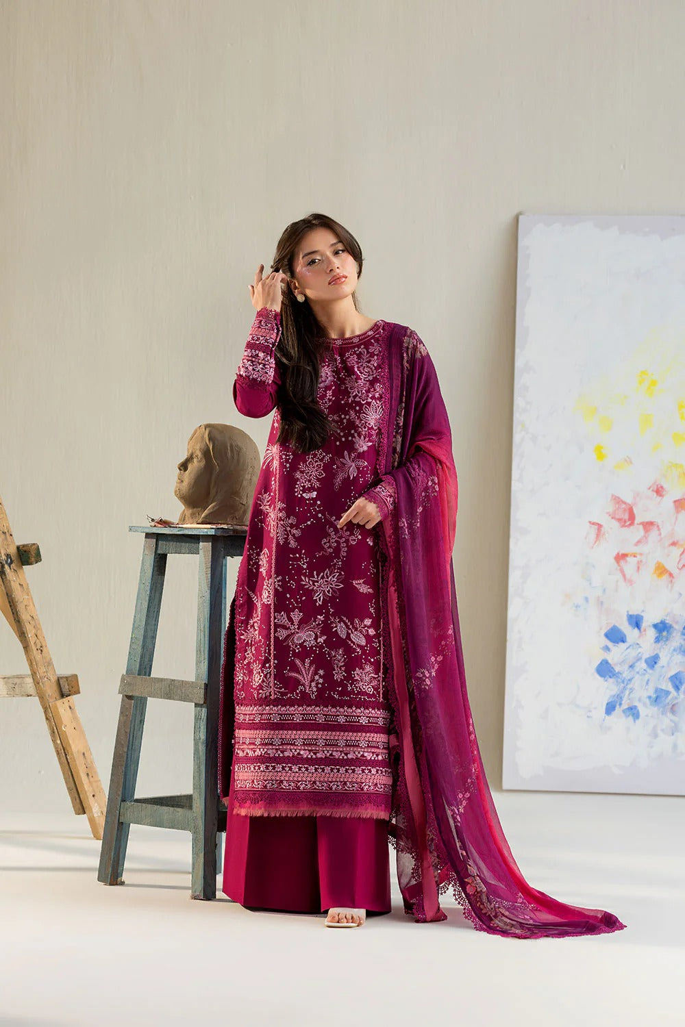 Woman in a magenta traditional outfit standing in a minimalistic room with a painting on the wall.