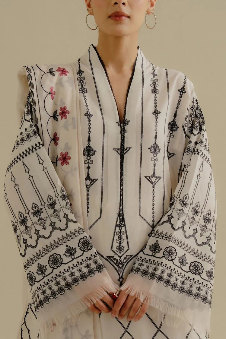 Woman wearing a white dress with black floral embroidery on a beige background