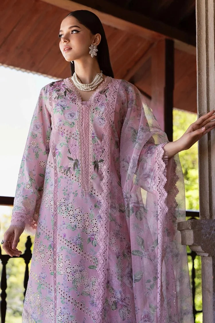 A woman models a light pink embroidered traditional outfit with floral patterns and lace details, standing on a wooden balcony.