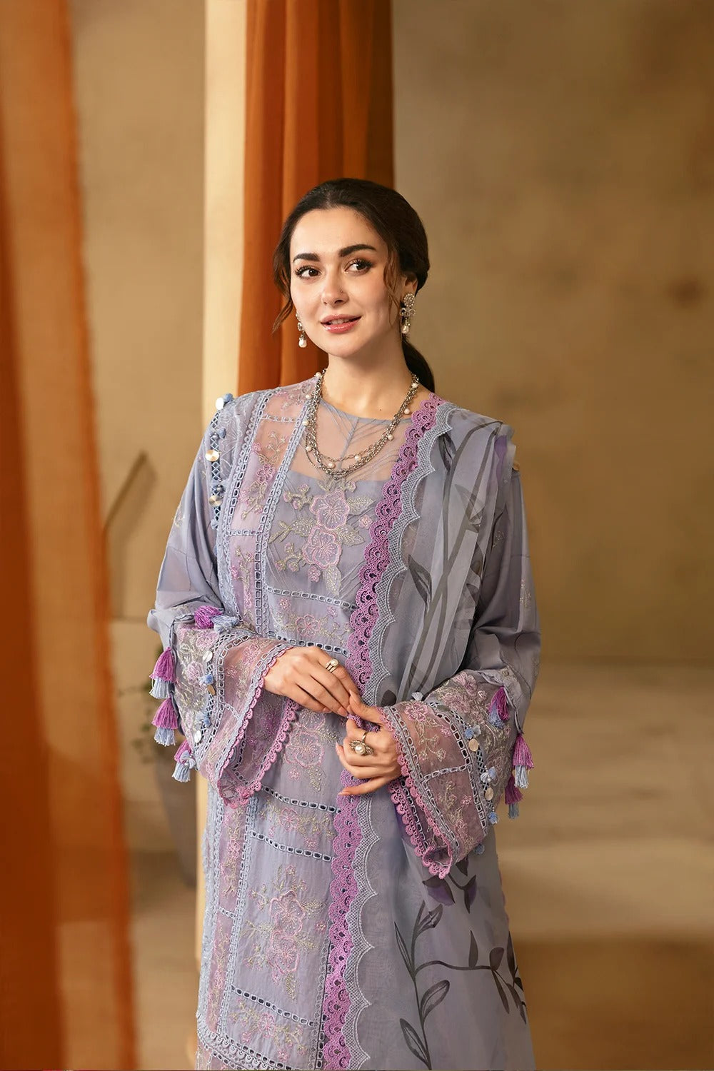 Woman wearing a gray and purple embroidered outfit with a neutral background