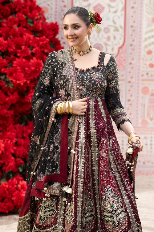 A woman models an ornate traditional Indian anarkali suit with heavy embroidery. The outfit features a black upper section with gold embroidery and a deep maroon lower skirt with intricate gold and silver embellishments.
