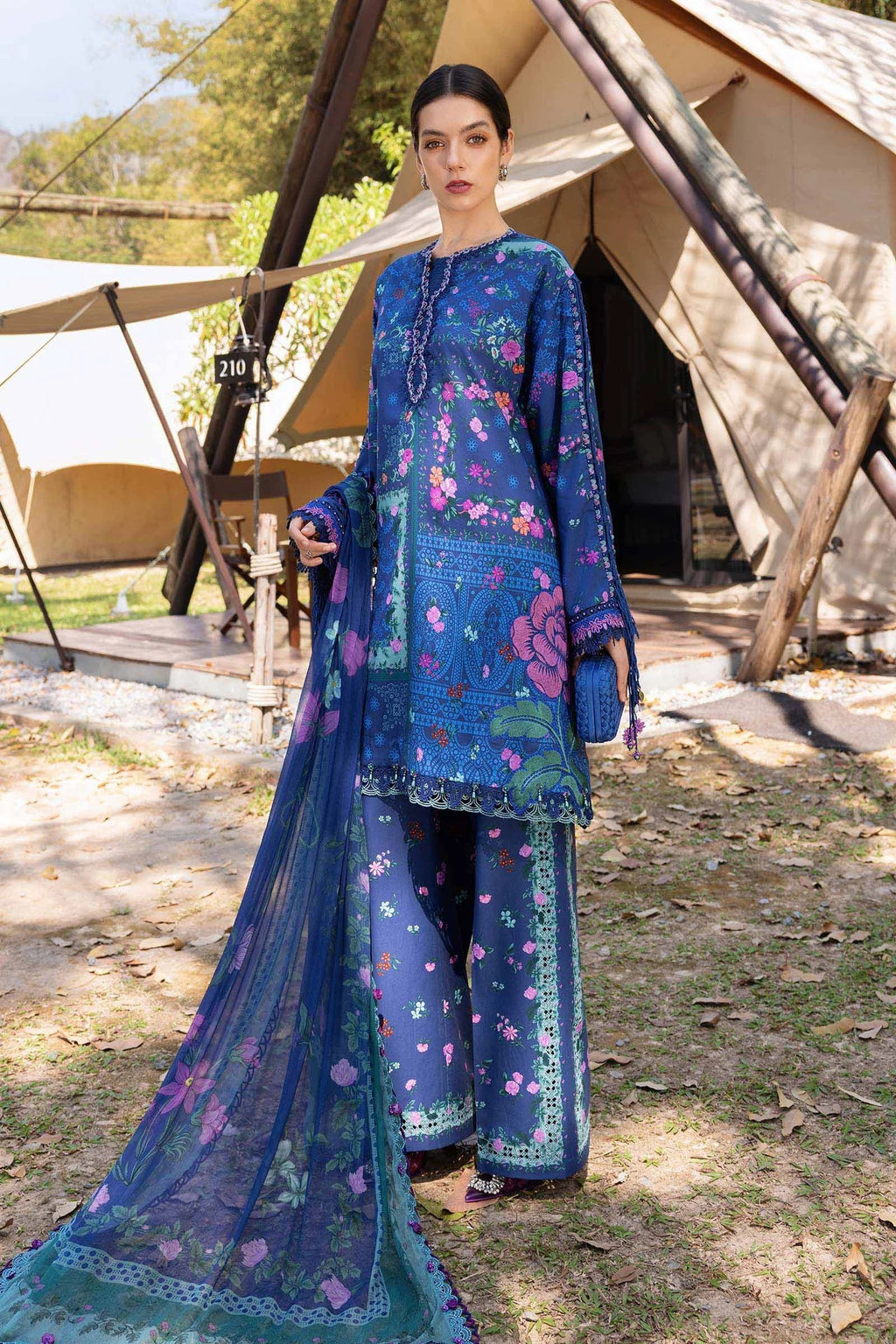 Woman in a blue embroidered traditional outfit standing in front of tents.