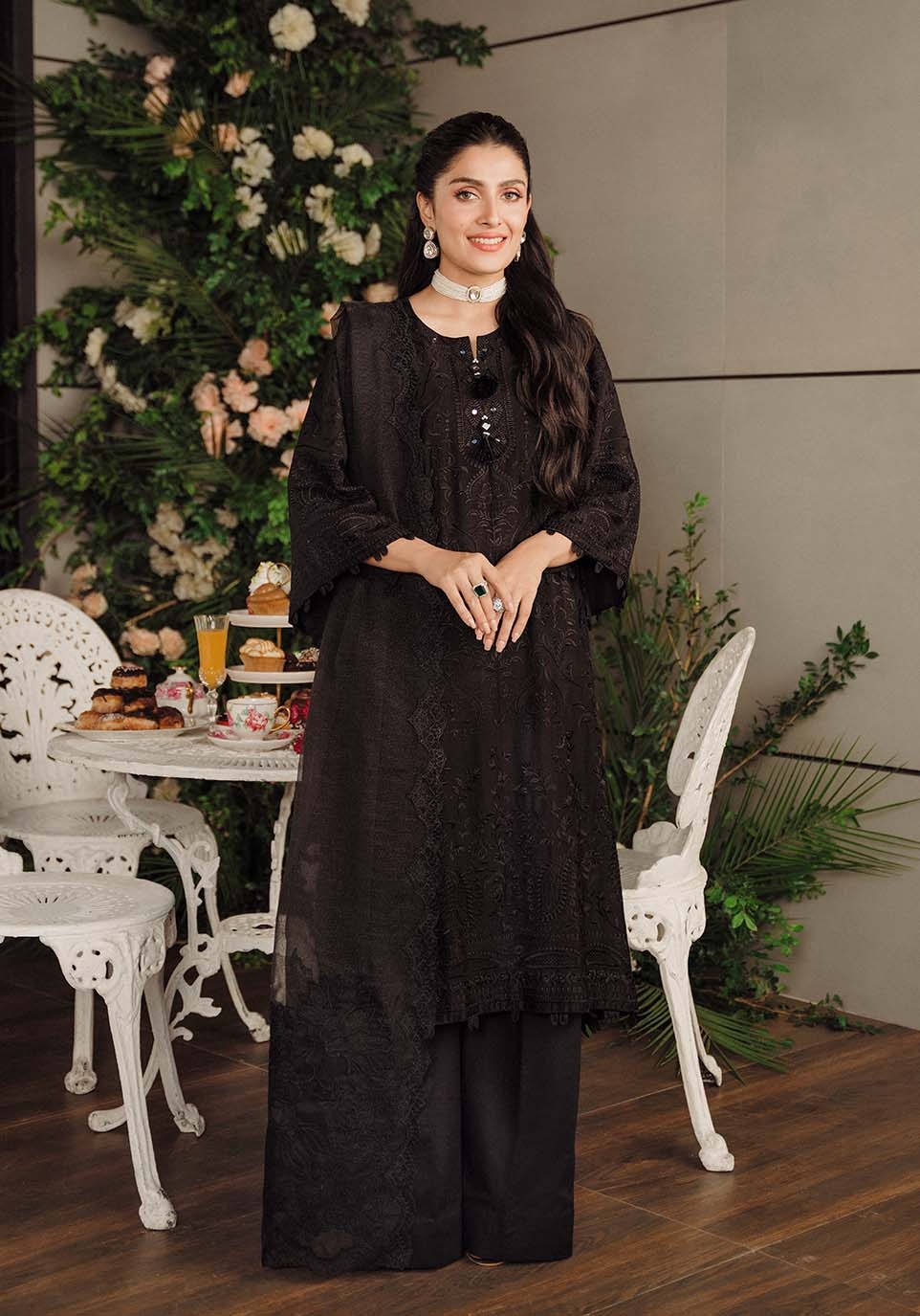 Woman in a black outfit standing in a decorated room with floral arrangements and a table.