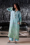 A woman models a light blue-green traditional outfit with floral embroidery, standing in front of a silver tinsel curtain and a black leather sofa.