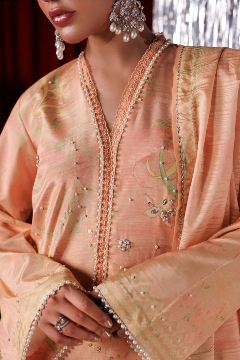 A close-up of a peach-colored embroidered traditional outfit with pearl bead trim, floral embroidery, and a matching dupatta, worn by a model with ornate silver earrings.