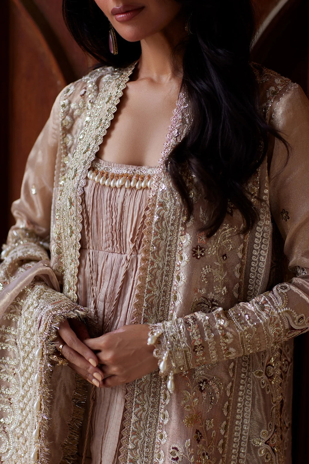 A close-up of a woman wearing an ornate beige and gold traditional outfit with intricate embroidery, a matching inner dress, and a draped shawl.