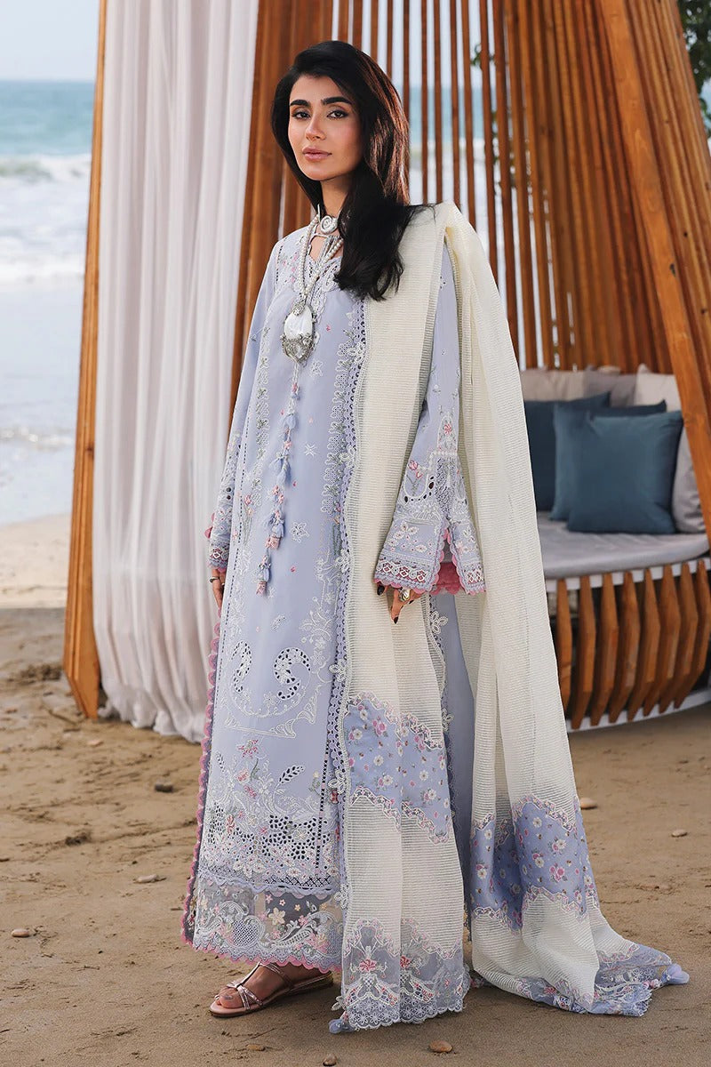 Woman in a light blue embroidered dress standing on a beach with ocean view.
