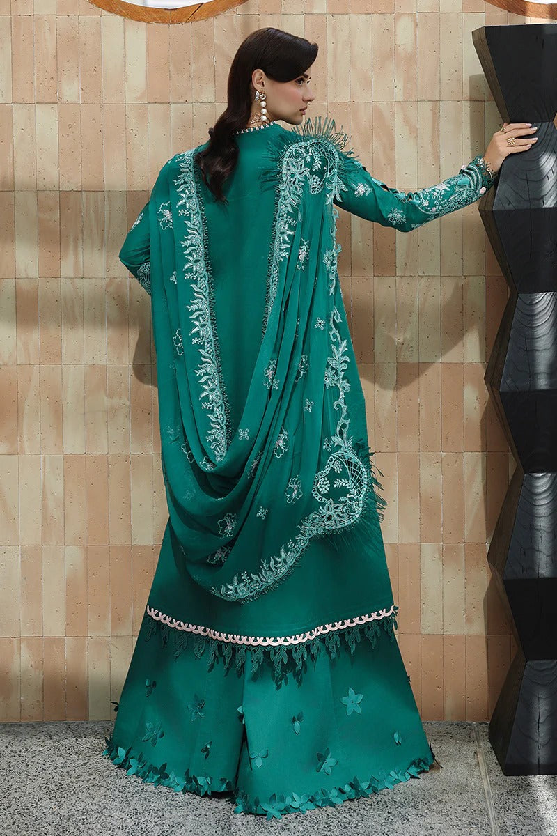 Woman in a green traditional outfit with intricate embroidery against a beige wall.