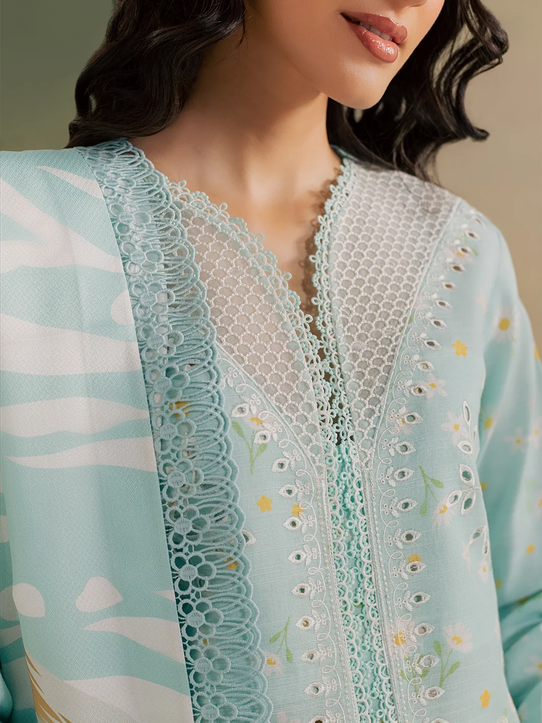 A woman shown from the back wearing a light blue embroidered kurta with a matching floral printed dupatta and white pants, standing against a soft gradient studio background.