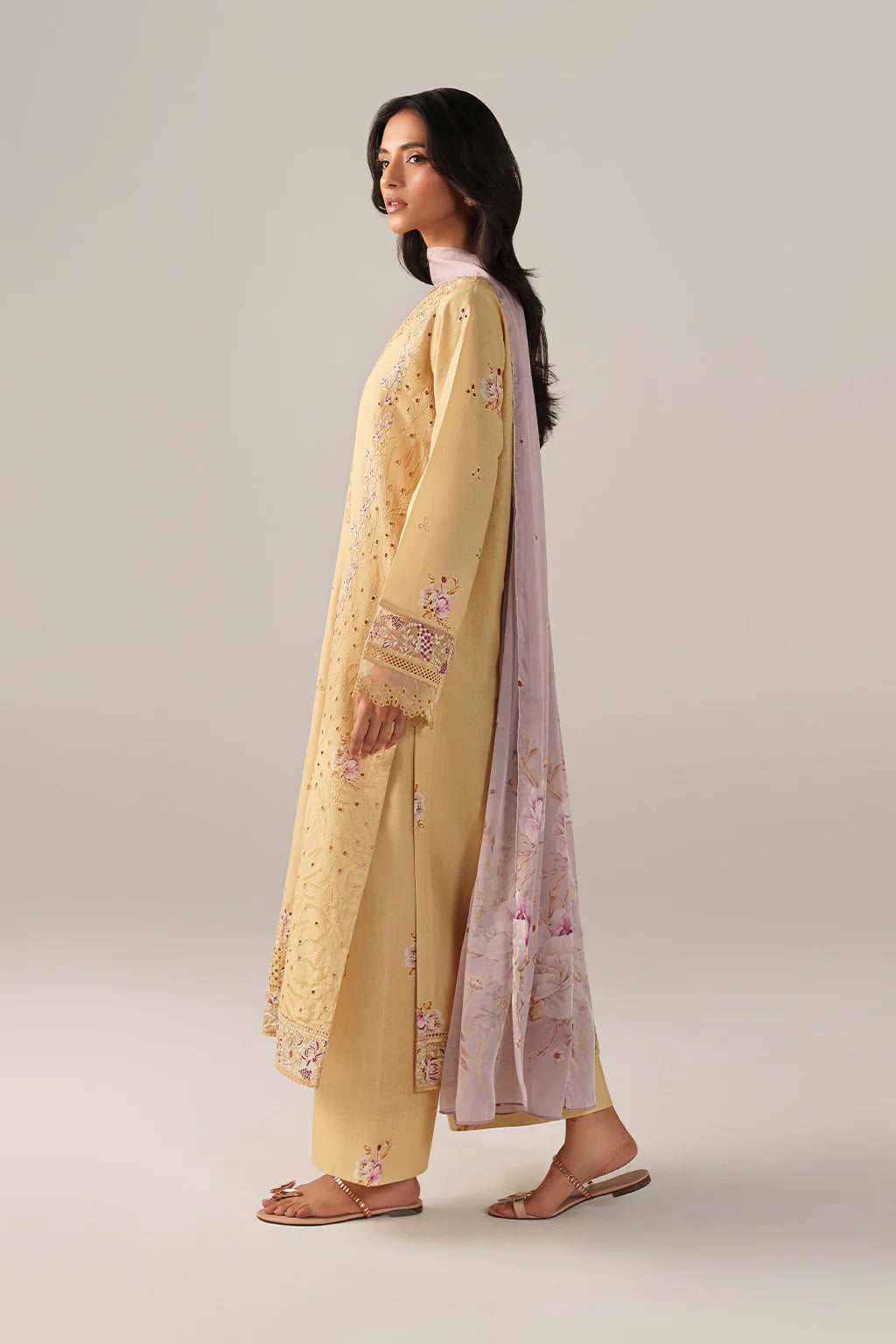 Woman wearing a yellow embroidered outfit with a matching dupatta on a beige background