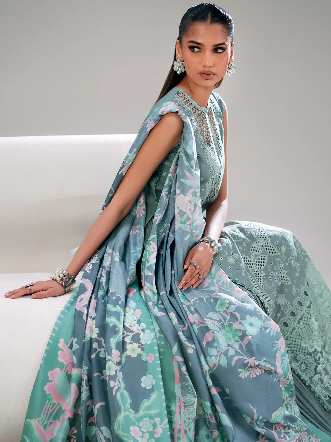 Woman wearing a light blue saree with floral patterns on a white couch.