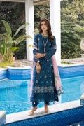 Woman in a blue embroidered outfit standing by a pool with greenery in the background