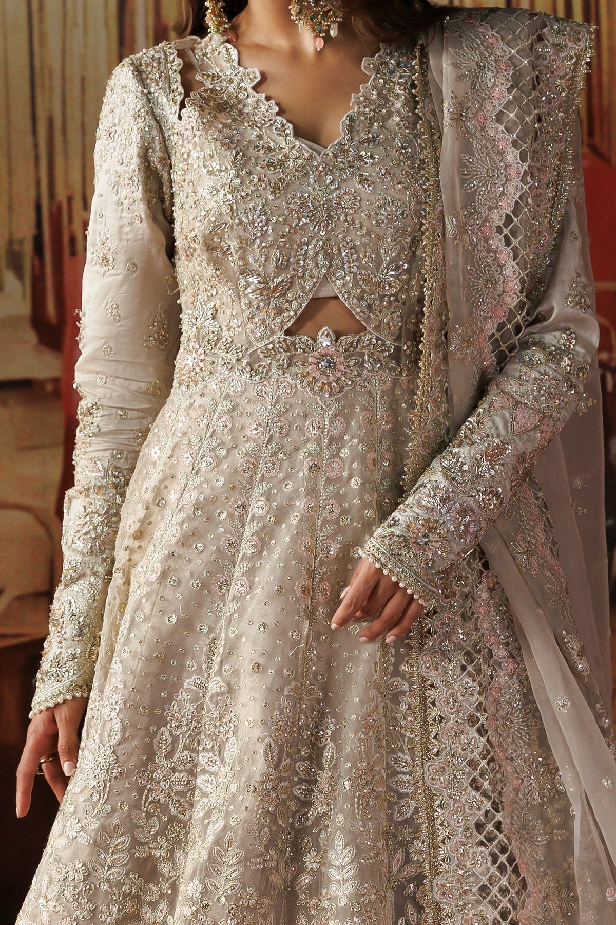 A close-up of a woman wearing an ornate cream and silver embellished traditional outfit with a heavily decorated long-sleeve kurta, matching skirt, and sheer embroidered dupatta.