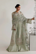 A woman models a light sage green embroidered traditional outfit with a matching dupatta, featuring intricate silver mirror work and floral embroidery, set against a minimalist studio background.