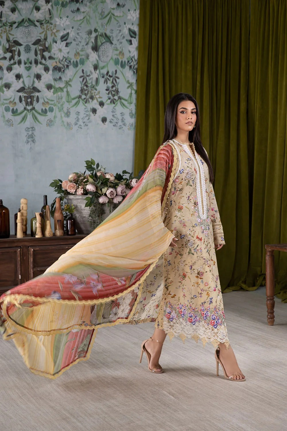 Woman in a floral dress with a flowing fabric in a decorative room.