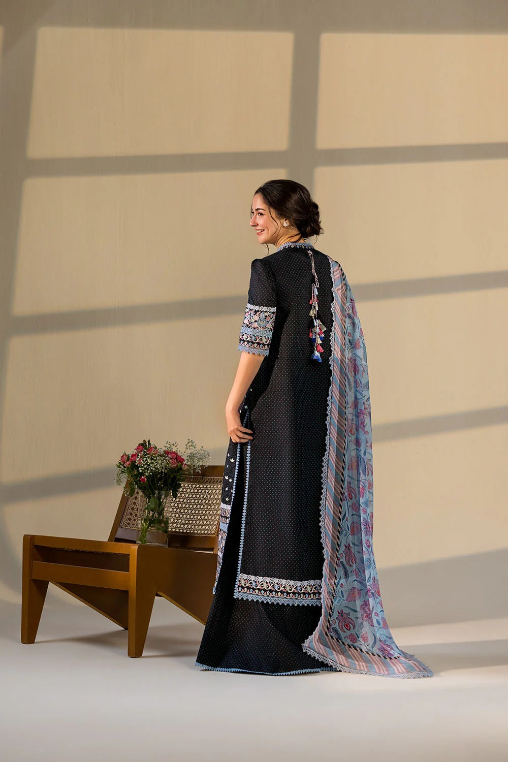 Woman in a black saree with a floral pattern standing in front of a beige wall.