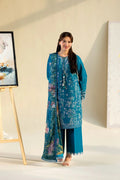 Woman wearing a blue embroidered outfit standing in a minimalistic room.