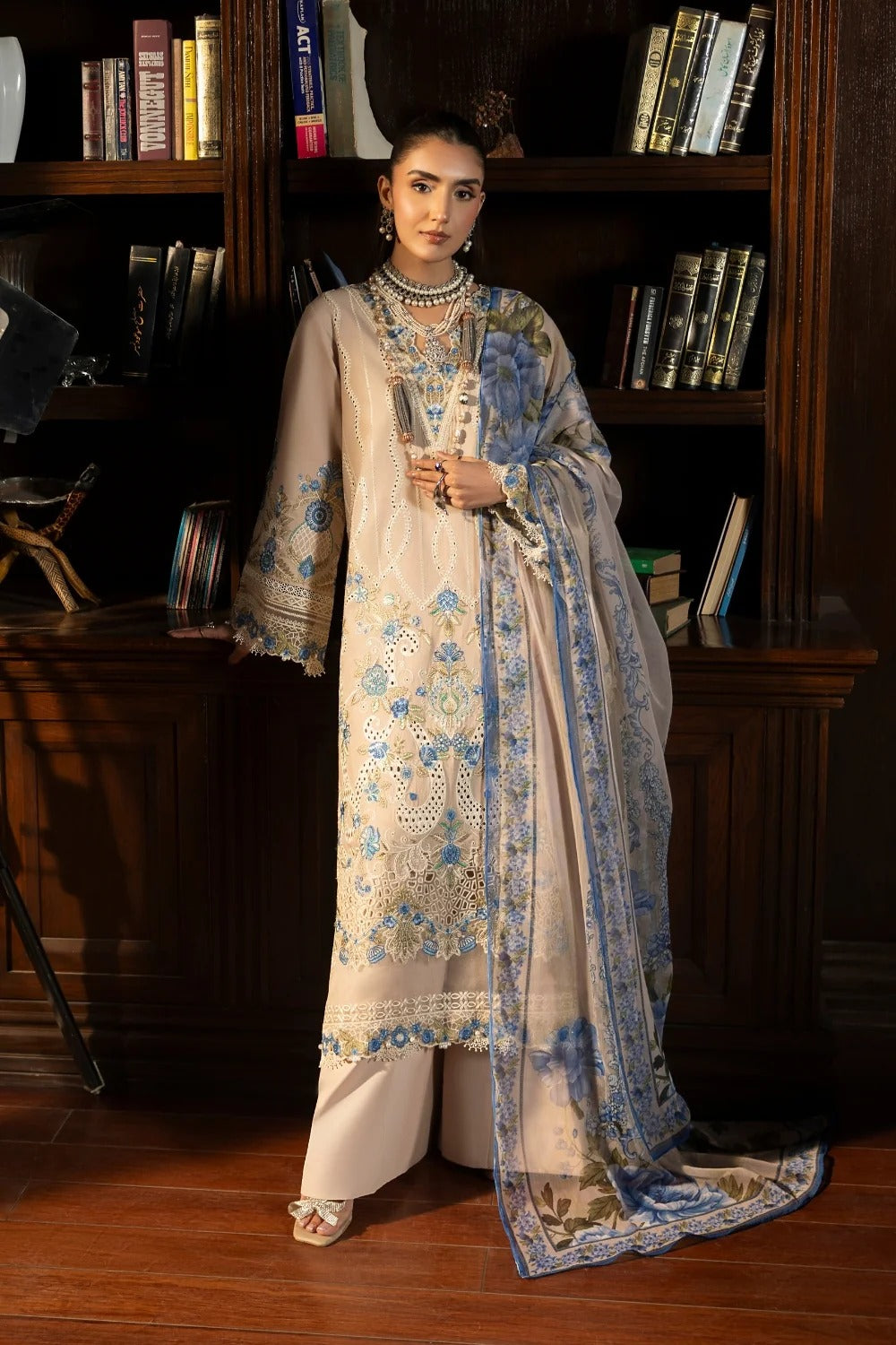 Woman in a traditional outfit with floral patterns standing in front of a bookshelf.